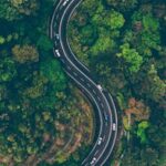 A sweeping aerial view of an S-shaped road winding through vibrant green Malaysian forest.
