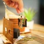 Close-up of hand holding a house key with a wallet and coins, symbolizing real estate investment.