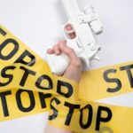 White toy gun held by hand wrapped with yellow stop tape, representing a call for nonviolence.