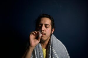 Close-up of a young man comfortably smoking in a dimly lit room, reflecting relaxation.