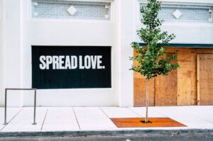 Street view with 'Spread Love' mural and a young tree on a sidewalk.