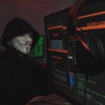 A person wearing a Guy Fawkes mask engaged in hacking activities on a computer in a dimly lit room.